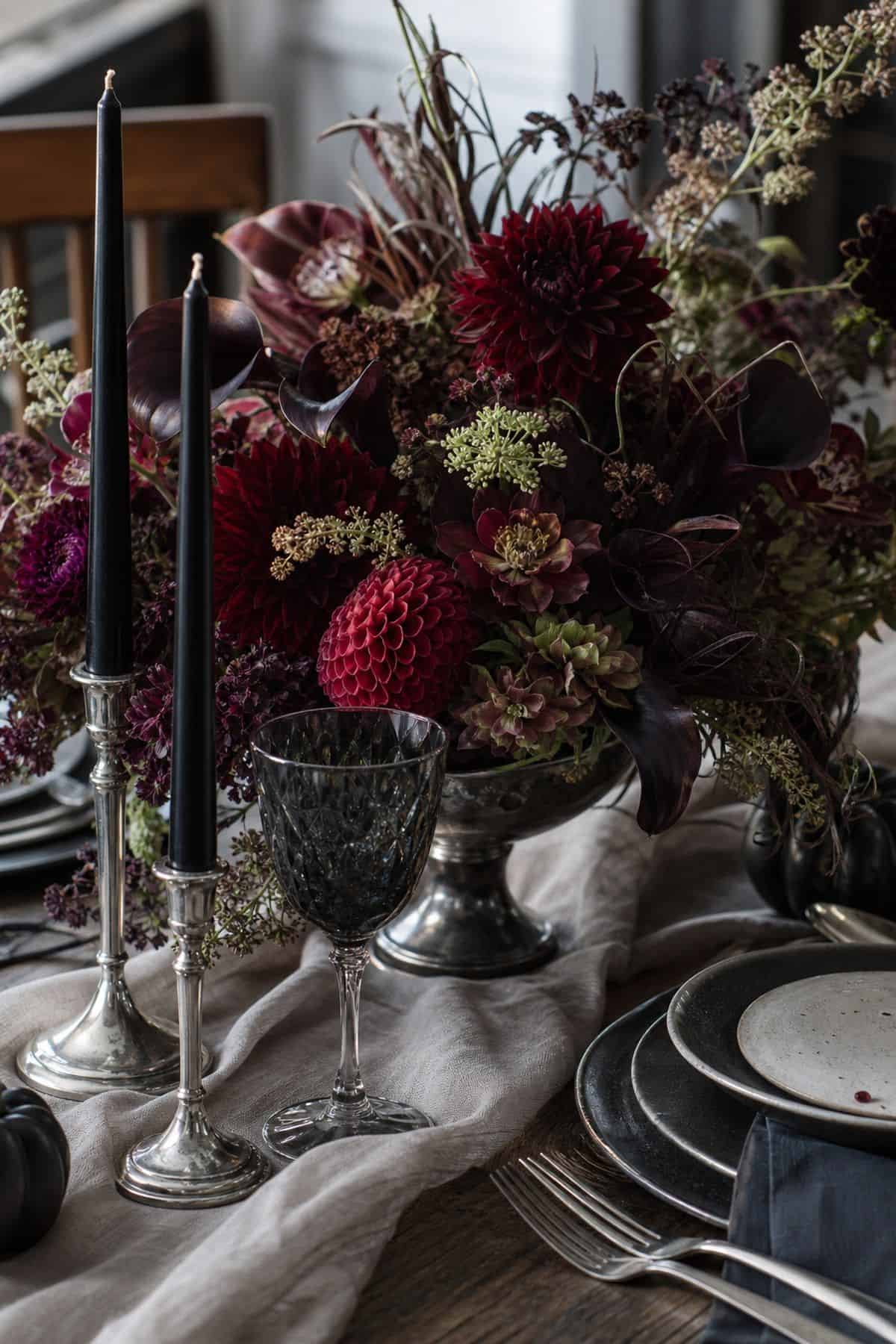 Dark floral Halloween centerpiece with burgundy flowers, black candles, and smoky glassware