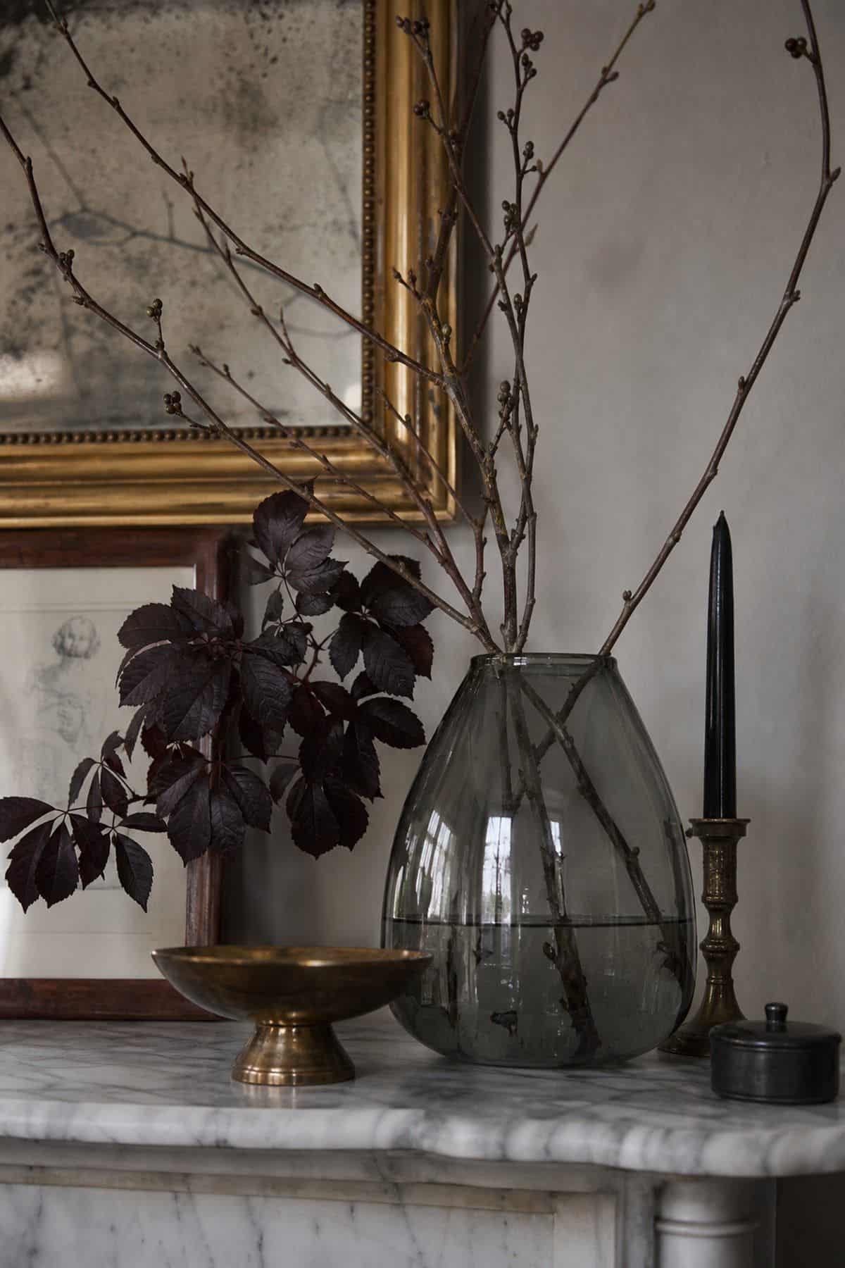 Smoky glass vase with dark branches styled on an elegant Halloween console table