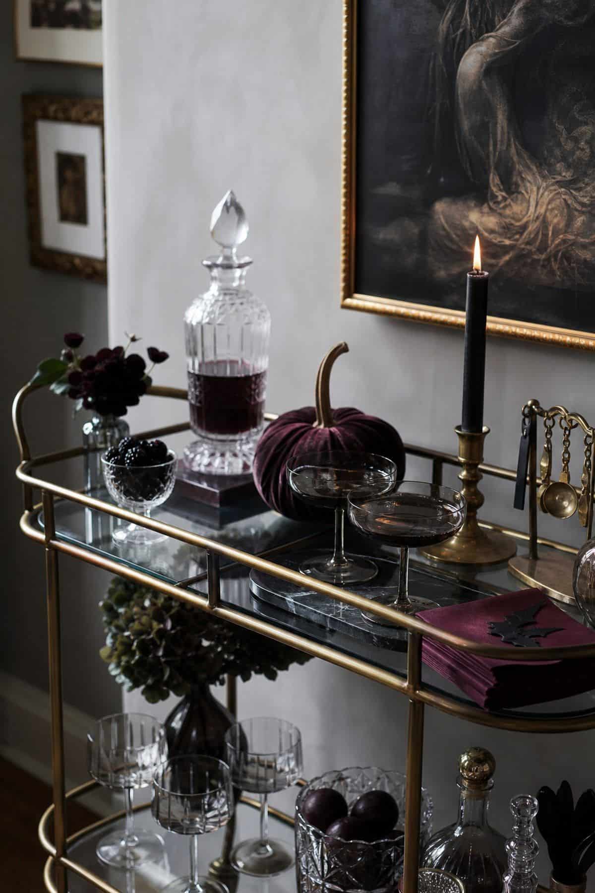 Brass bar cart with subtle Halloween styling, smoky glasses, and a velvet pumpkin