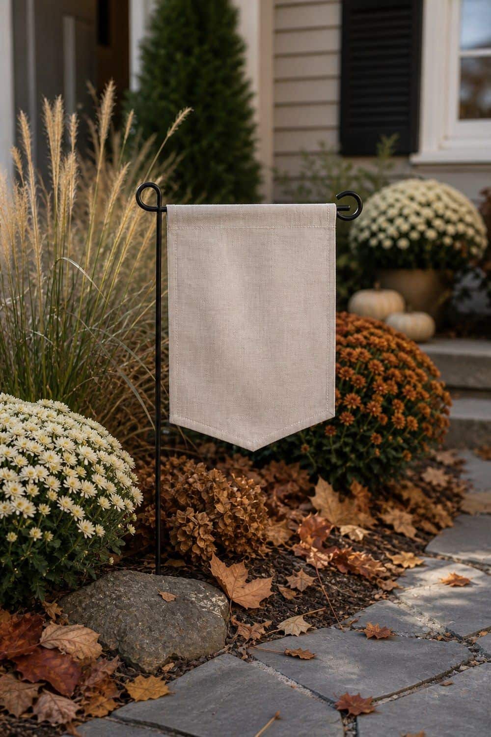 Plain cream linen garden flag on a black stand in a bed of white and rust mums and ornamental grasses