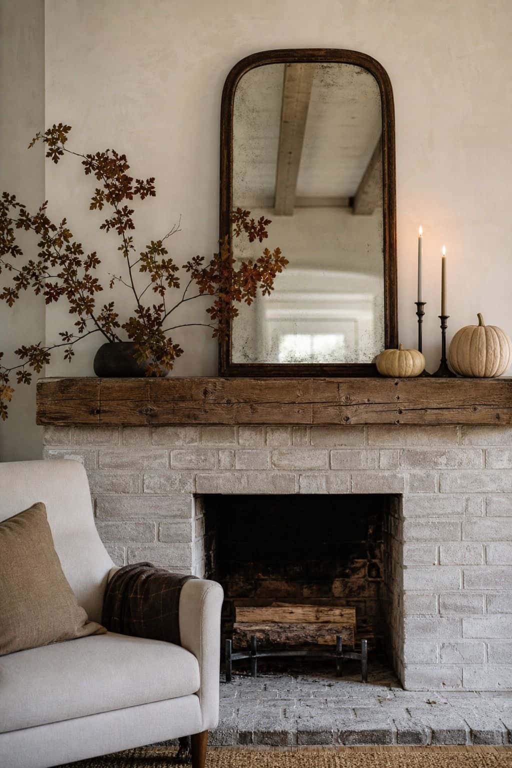 White painted brick fireplace with a wood beam mantel, an arched mirror, one branch arrangement, two black candlesticks and small white pumpkins