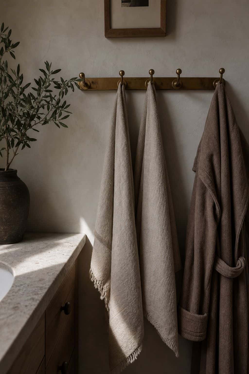 Warm brass hook row holding towels and a robe on a textured bathroom wall.