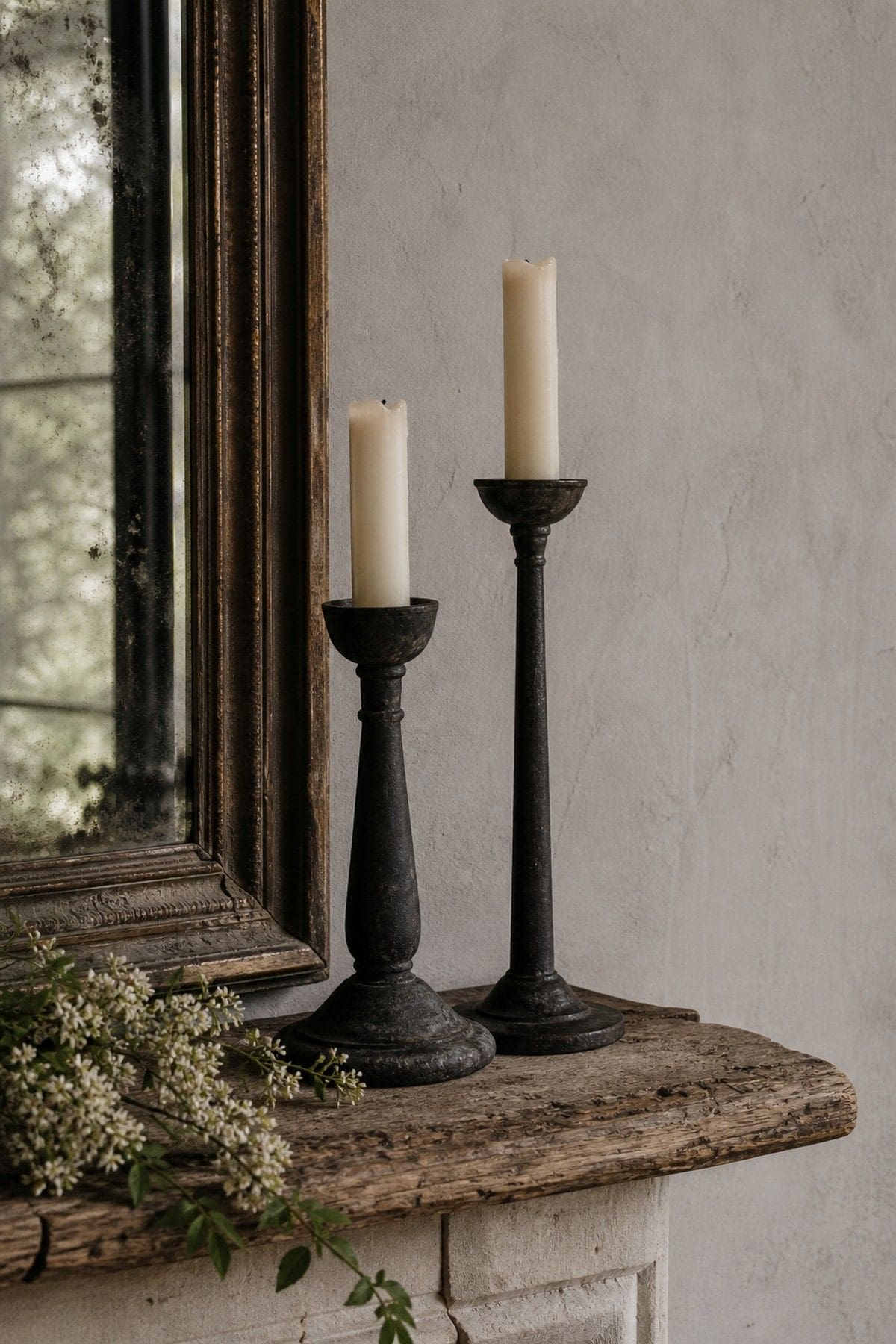 Black iron candle holders arranged on a rustic French country mantel.