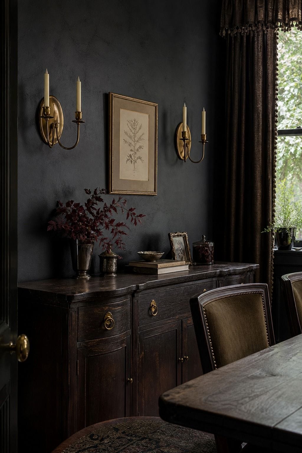 Antique brass wall sconces on a charcoal wall with candles, botanical art, and dark wood.