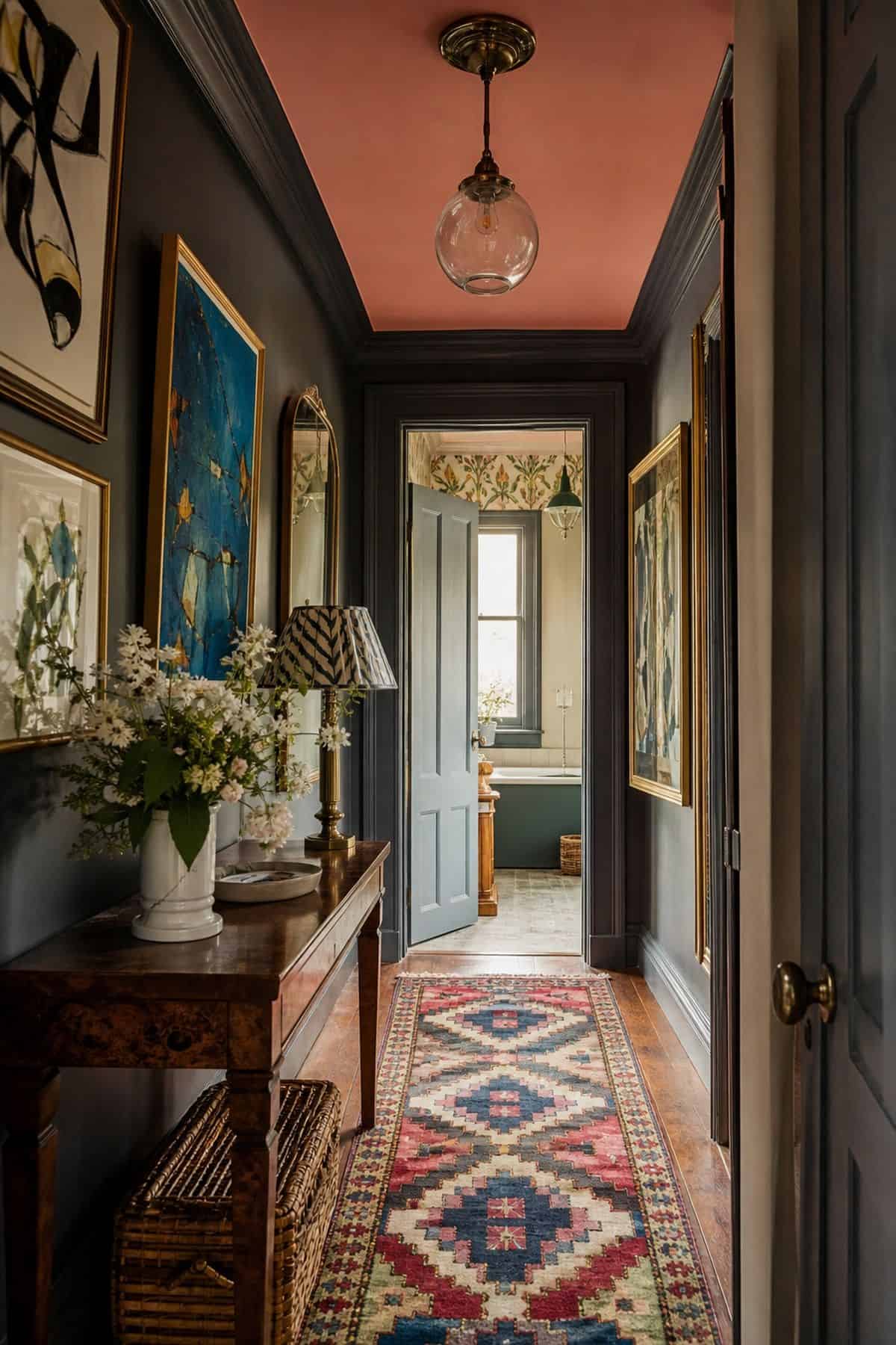 7. A Runner With Personality styled for a maximalist rug ideas article, shown as realistic editorial interior photography with a narrow maximalist hallway with a bold patterned runner, colorful framed art, painted trim, vintage console table, flowers, and warm natural light. The image emphasizes how the rug shapes the whole room through color, pattern, scale, and layered texture while still feeling lived in and attainable. Soft natural daylight, imperfect vintage details, books, art, textiles,