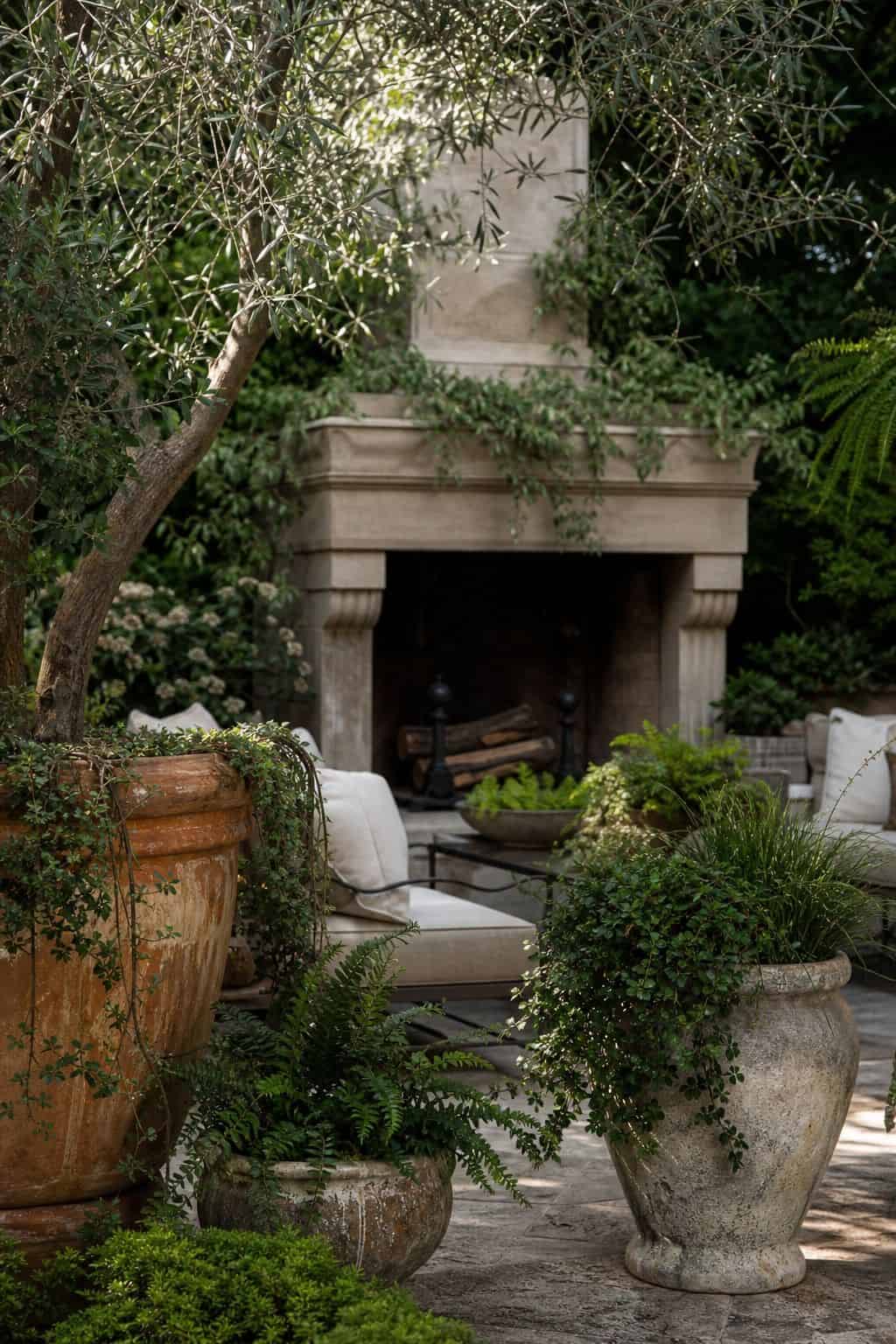 Surround the space with large potted plants or lush greenery shown as a realistic Pretty Wild World image for 15 Outdoor Fireplace Patio Decor Ideas for an Effortless Outdoor Living Aesthetic.